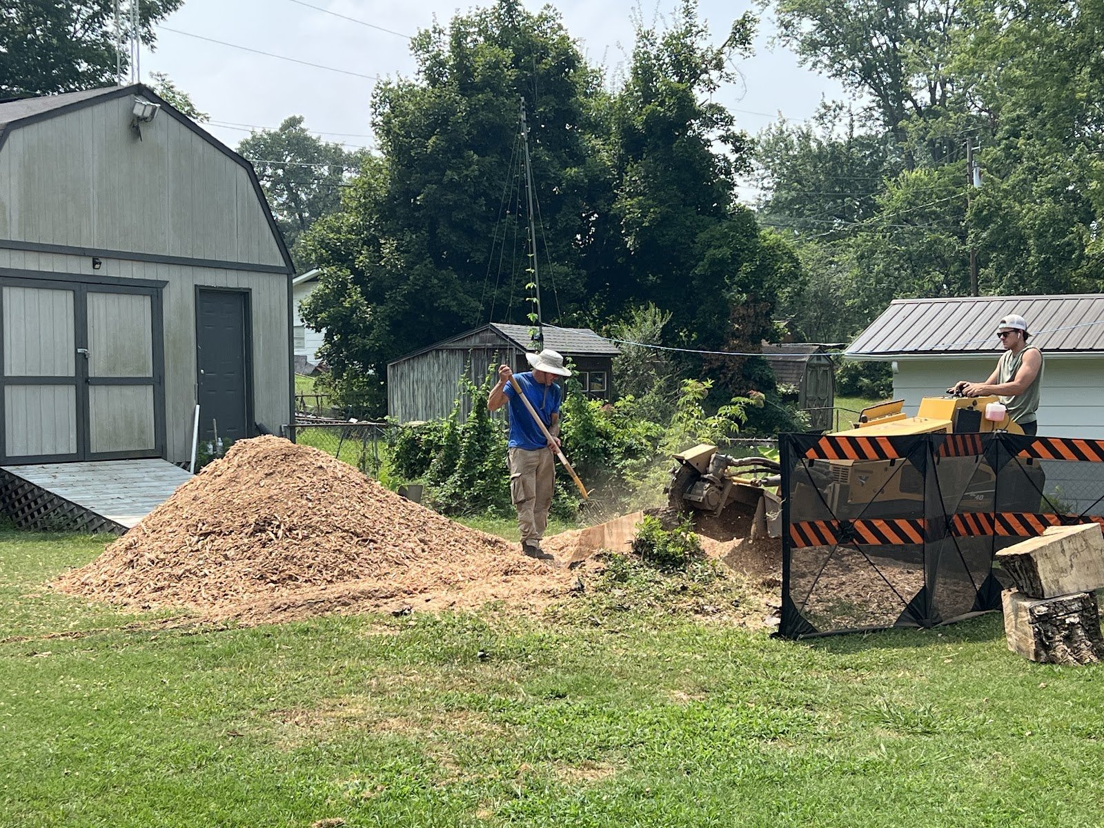 Stump grinding next to a barn with a grinder and a pile of wood chips